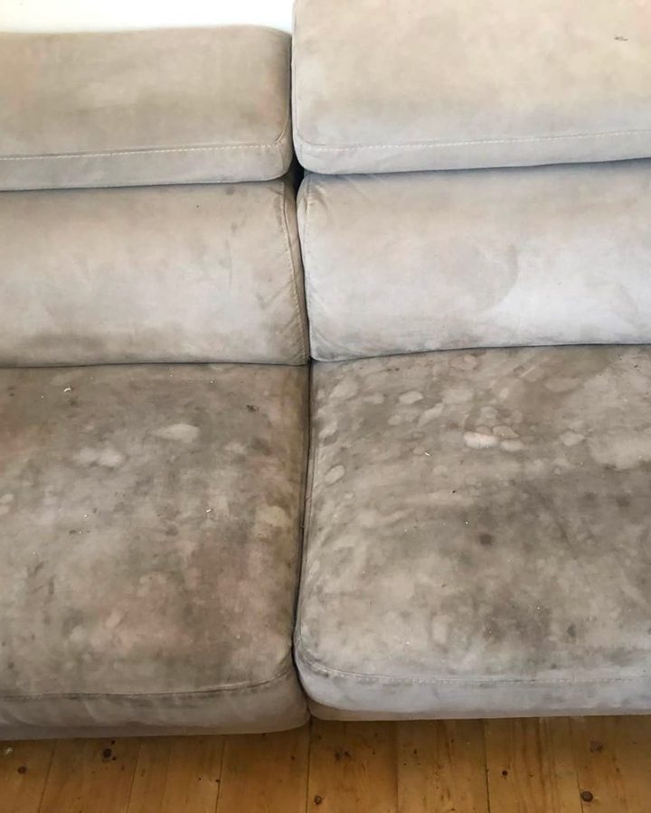 A grey suede sofa with dark marks across the seat cushions