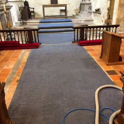 A church aisle carpet being cleaned between rows of red chairs